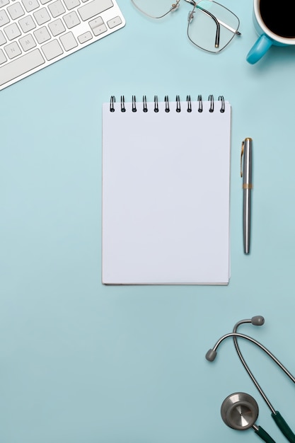 Notebook, stethoscope, glasses and coffee cup on blue background.