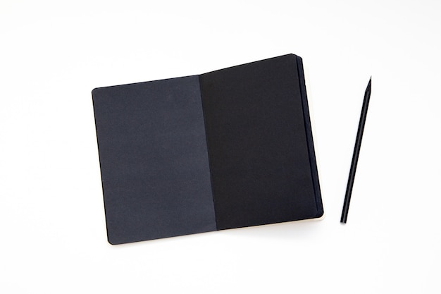 Notebook with black paper and pencil on white background.