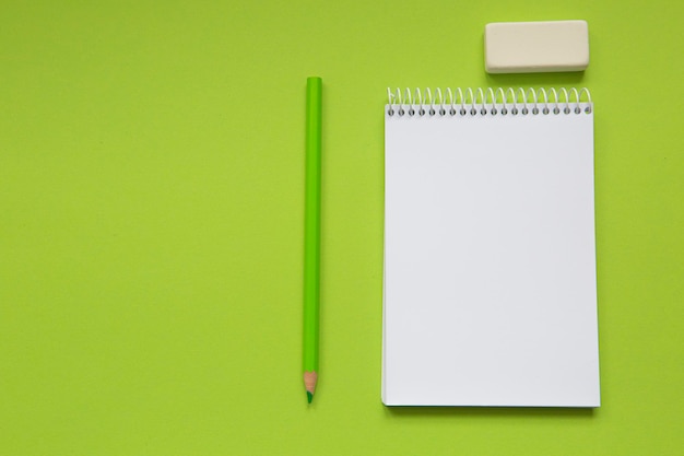 Notebook with a blank page on a pistachio green background and together with a pencil and various st