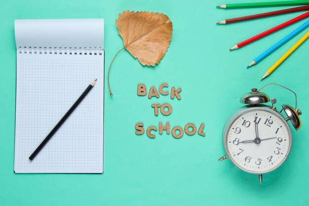 Notebook with colored pencils and alarm clock isolated on blue