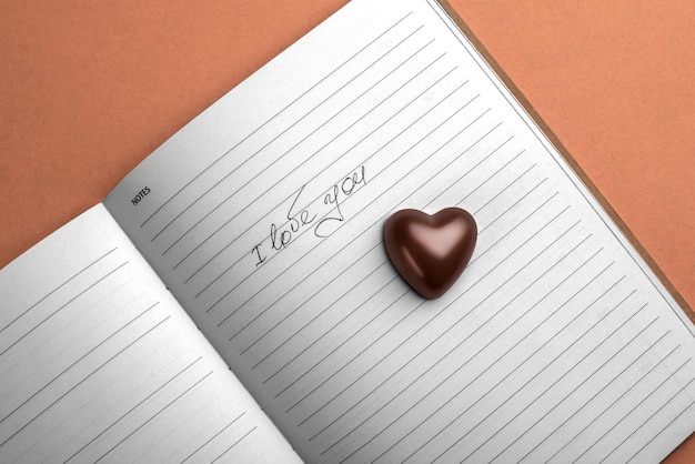 Photo notebook with the inscription i love you on a brown background with a heartshaped chocolate candy