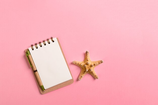 Notebook with sseashells on pink background top view flat lay. Planning summer holidays, tourism and vacation concept