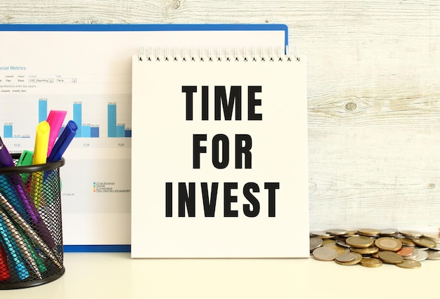 A notebook with the text TIME FOR INVEST is leaning against the wall with a folder with charts