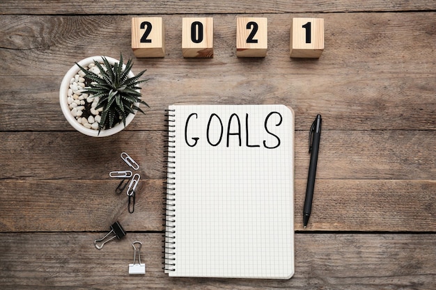 Notebook with word Goals near number 2021 made of cubes new year aims Objects on wooden table flat lay