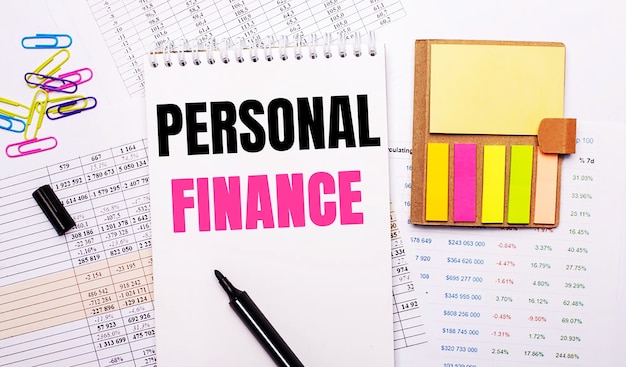 Photo a notebook with the words personal finance, a marker, colored paper clips and bright note paper lie on the background of the graphs