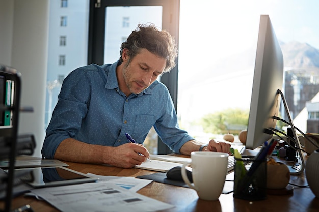 Notebook writing and planning with a businessman working on his desk in the office for growth or development Strategy mindset and mission with a male employee at work to write notes in his book