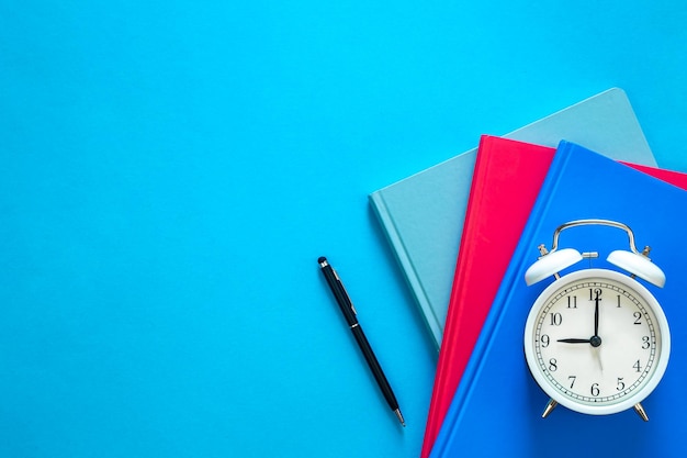 Notebooks pen and alarm clock on a blue background top view