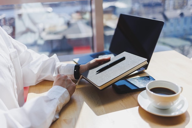 Notepad for entries in female hands on the background of a laptop closeup a cup of coffee on a wooden table Businessman's desk Working process selective focus