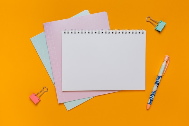 Notepad, exercise book and pen on the desk. Mock up in copy space office on orange background. Back to school