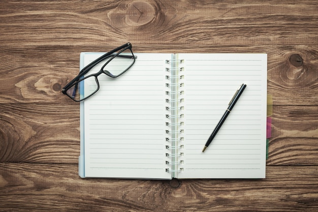 Notepad glasses and pen on a wooden background.