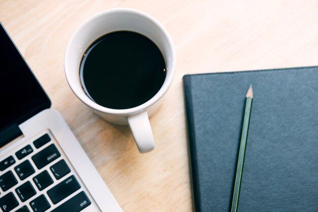 Notepad, laptop and coffee cup on wood table with top view.