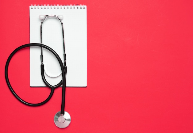 Notepad and medical stethoscope on a red background