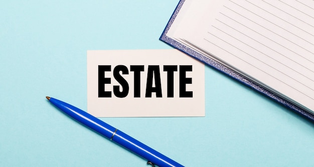 Notepad, white pen and card with the inscription ESTATE on a blue background. View from above