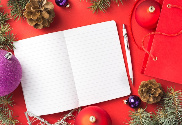 Notepad with Christmas decorations on red desktop top view