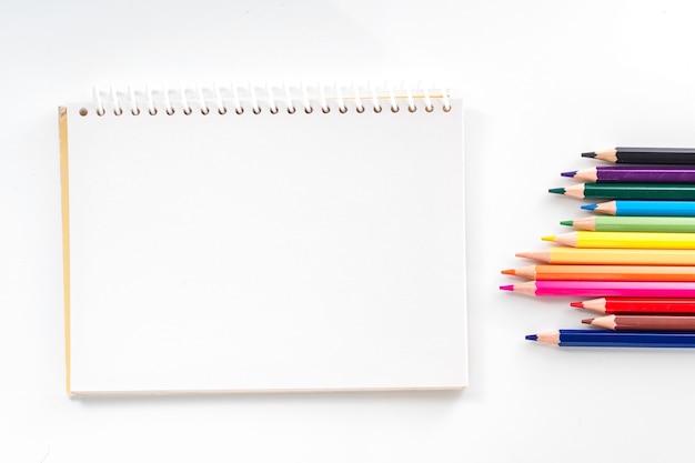 Notepad with color pencil on white table view from above