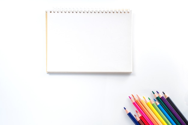 Notepad with color pencil on white table view from above