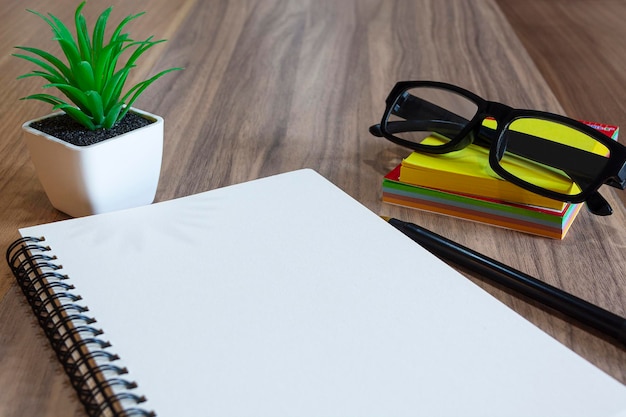 Notepad with glasses pen colorful stick note and potted plant on wooden desk flat lay