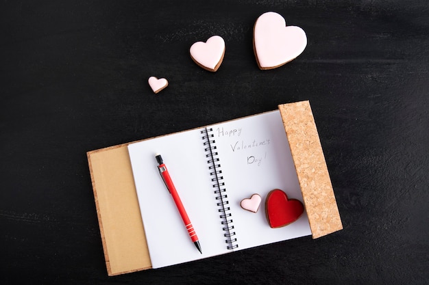 Photo notepad with inscription happy valentines day on black background with white and red hearts.