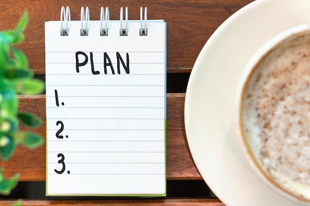 Notepad with the inscription plan and a cup of coffee on a wooden background top view.