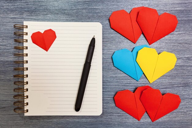 Notepad with multi-colored hearts and a pen lay on a table. Notepad with hearts.