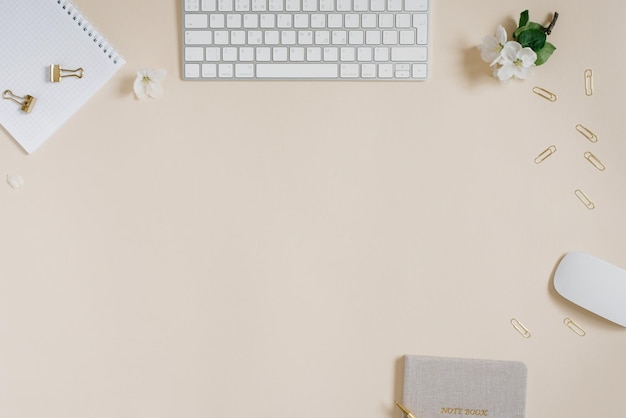 Notepad with a pen a branch with green leaves and white flowers and a laptop keyboard