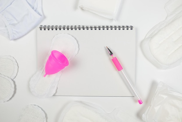 Notepad with pen pads menstrual cup and panties on white copy space place for text The concept of menstruation women's creative days