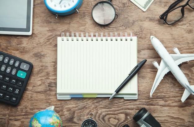 Notepad with pen and travel items on the wooden background.