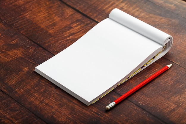 Notepad with red pencil on a brown wooden table background, for education, write goals and deeds