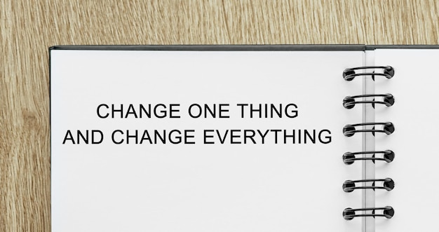 Notepad with text Change one thing and change everything on wooden deskt Business and finance concept