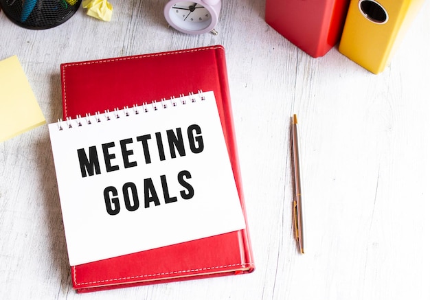 Notepad with the text MEETING GOALS on a wooden table Red diary and pen