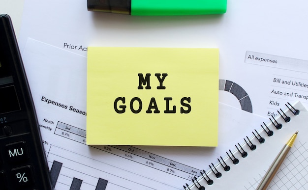 Notepad with text MY GOALS on a white background near pen and calculator