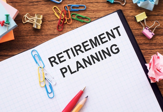 Notepad with the text RETIREMENT PLANNING on the table with colored paper clips and crumpled sheets