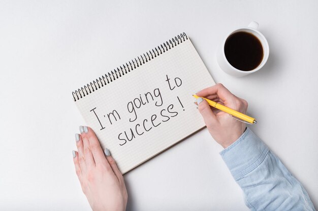 Notepad with words I am going to success Female hands with Cup of coffee and copybook White background