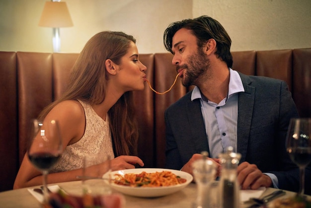 Nothing inspires romance quite like Italian food Shot of a young couple sharing spaghetti during a romantic dinner at a restaurant