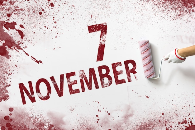 November 7th. Day 7 of month, Calendar date. The hand holds a roller with red paint and writes a calendar date on a white background. Autumn month, day of the year concept.