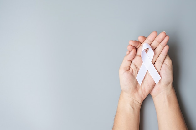 November Lung Cancer Awareness month, democracy and international peace day. Man holding white Ribbon on grey background