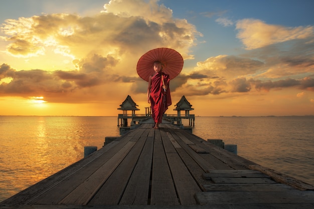 Novice boy walking on the wooded bridge with red umbrella