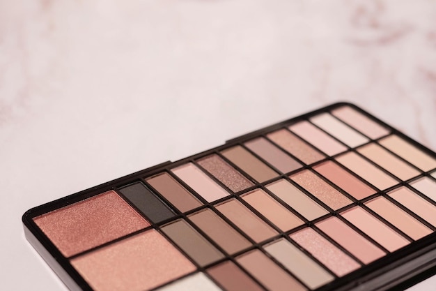 Nude eyeshadow palette in pink and beige on a blurred marble background with copy space.