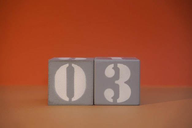 Number 03 on wooden grey cubes closeup Concept of date time Math concept Copy space for text or event White numbers 3 on building blocks orange background Educational cubes Selective focus