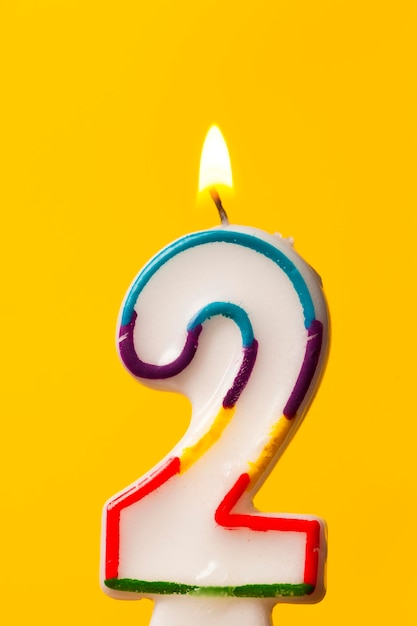 Number 2 birthday celebration candle against a bright yellow background