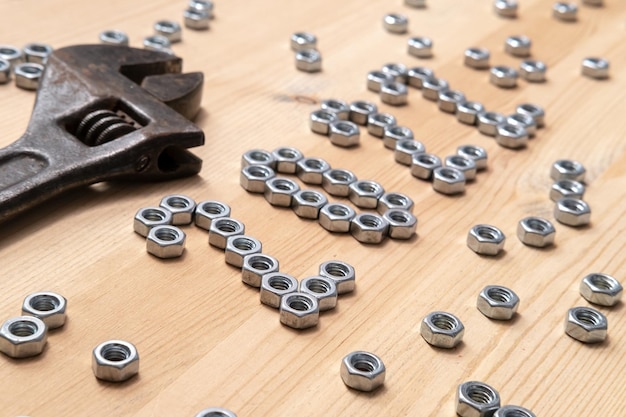 Number 2022 is lined with metal nuts on a wooden table next to a large old wrench