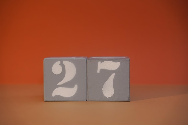 Number 27 on wooden grey cubes closeup Concept of date time Math concept Copy space for text or event White numbers 27 building blocks orange background Selective focus