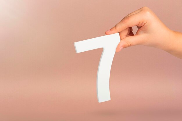 Number seven in hand hand holding white number on red background with copy space concept with number