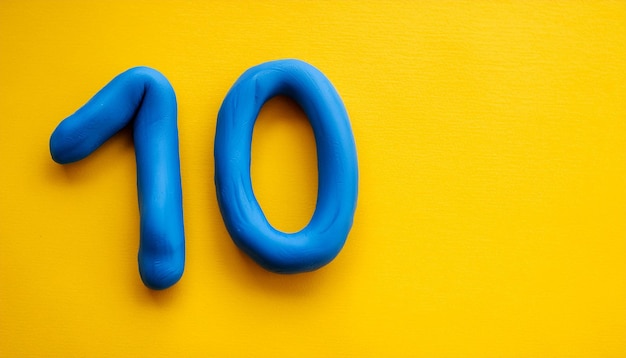 Photo numbers 10 made of blue plasticine on yellow background math learning development flat lay