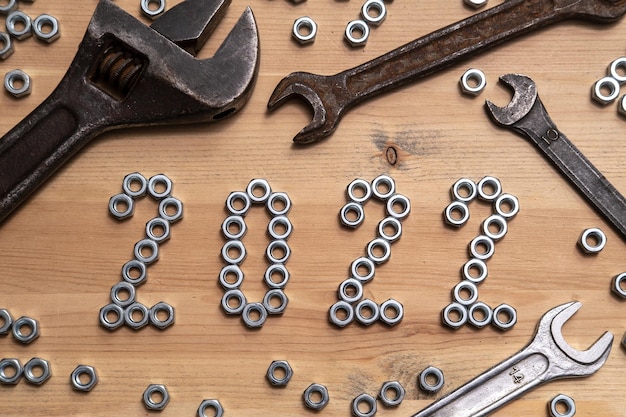 Numbers 2022 are lined with metal nuts on a wooden table next to a variety of wrenches