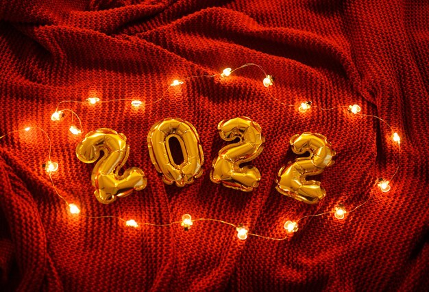 Photo numbers 2022 on the background of a red knitted cozy plaid and christmas lights.