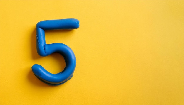 Photo numbers 5 made of blue plasticine on yellow background math learning development flat lay