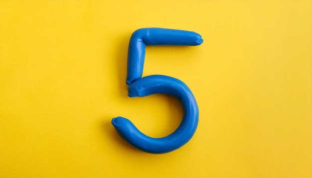 Numbers 5 made of blue plasticine on yellow background Math learning development Flat lay