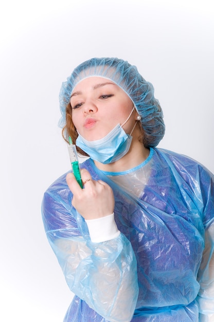 A nurse in a Bathrobe and mask looks at a syringe during a pandemic