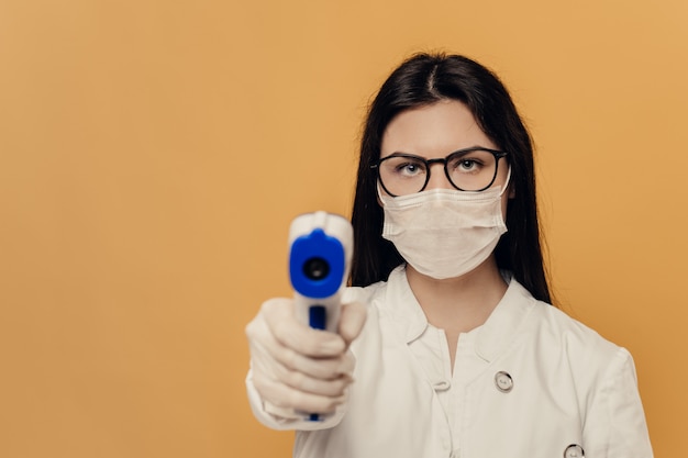 Nurse in glasses. surgical mask and protective gloves, holds thermometer, ready to test because of spread coronavirus pandemic.